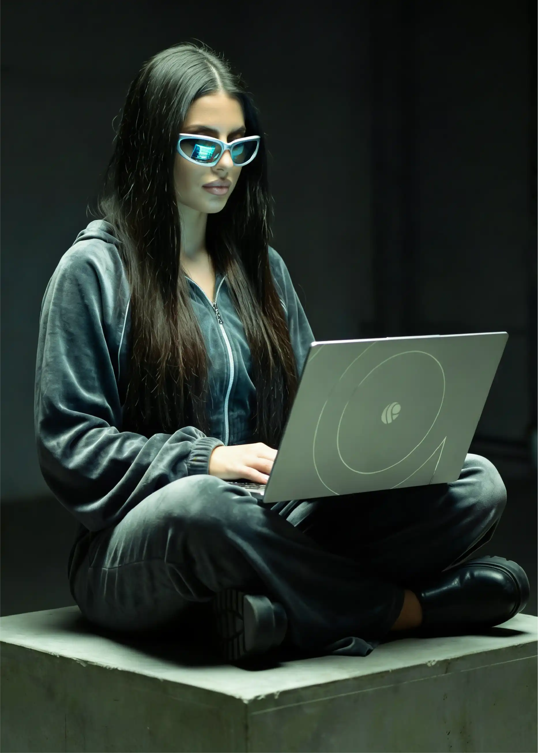 Coder in a grey tracksuit sitting cross-legged and typing on a Primebook laptop