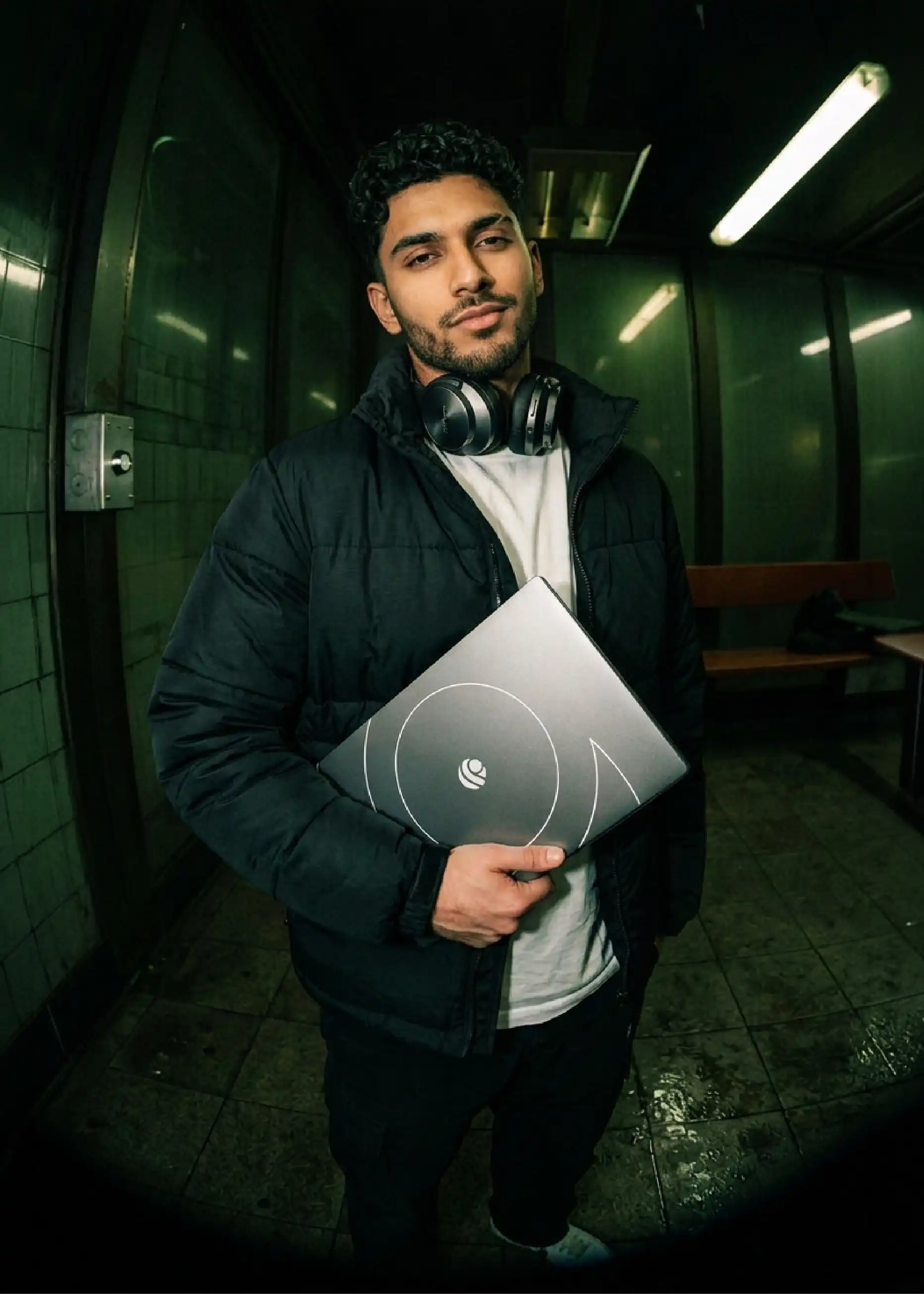 Professional in a black jacket holding a closed Primebook laptop at a subway station